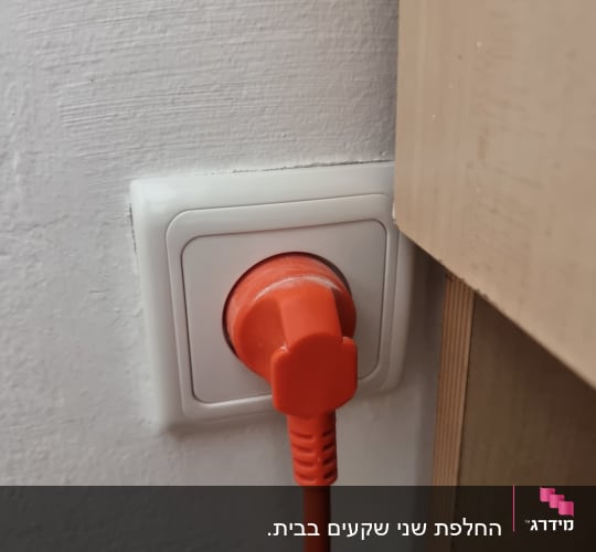 תקע כתום בשקע חשמלי על קיר לבן